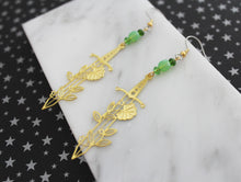 Gold steel laser cut sword charms with floral accents on the sword. Charms hang from steel fish hook ear wires. Earrings paired with glass Czech crystal beads.